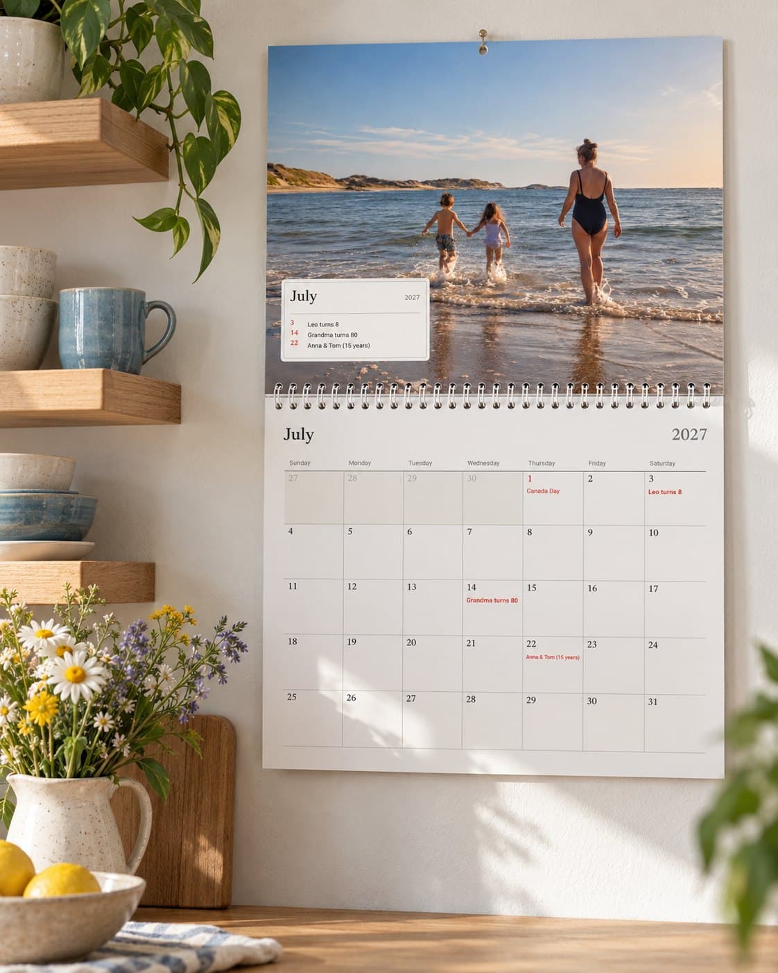 A photo calendar open at July in a bright kitchen: a family's beach photo above the month with their birthdays