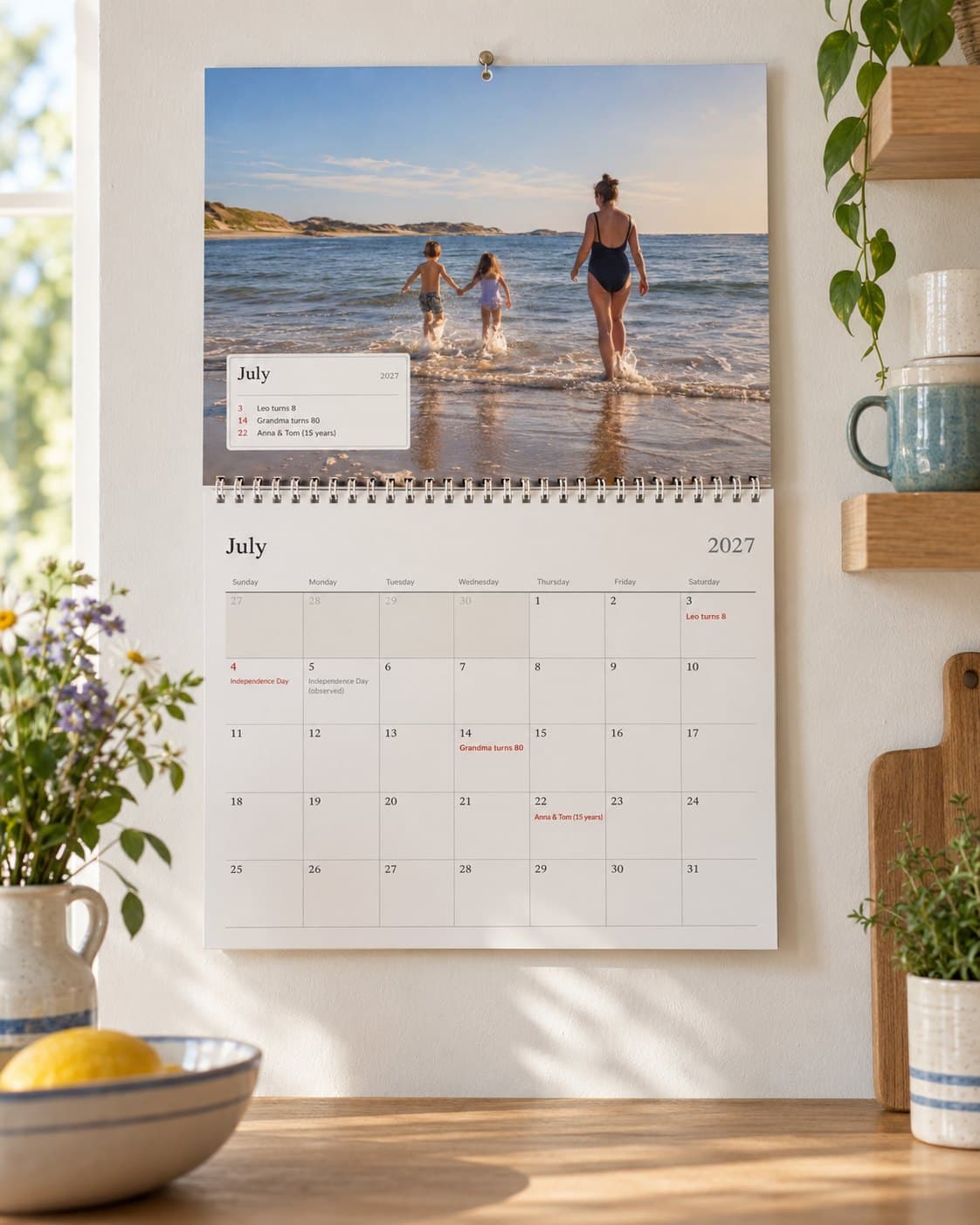 A photo calendar open at July in a bright kitchen: a family's beach photo above the month with their birthdays
