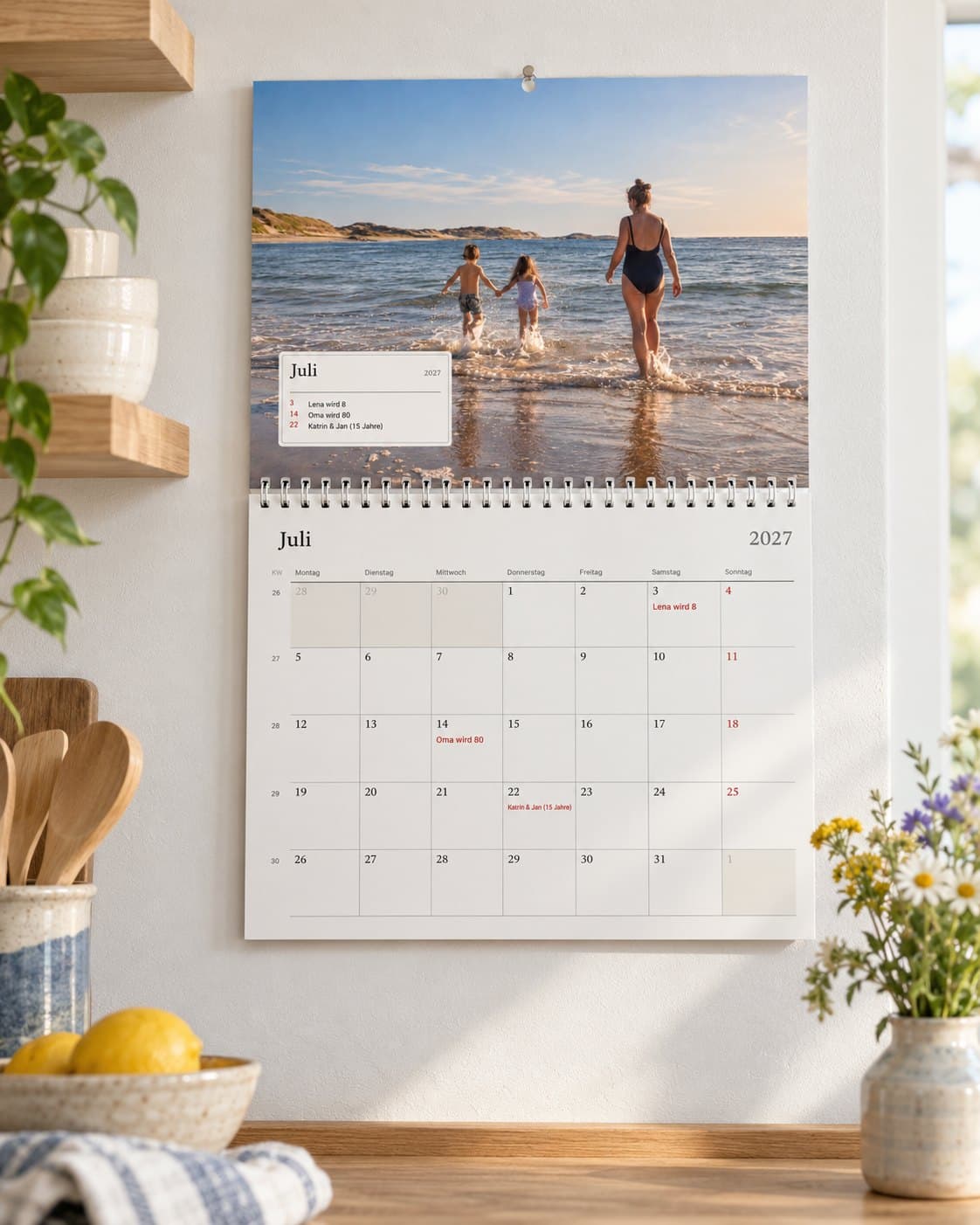 Ein Fotokalender, aufgeschlagen im Juli in einer hellen Küche: das Strandfoto der Familie über dem Monat mit ihren Geburtstagen