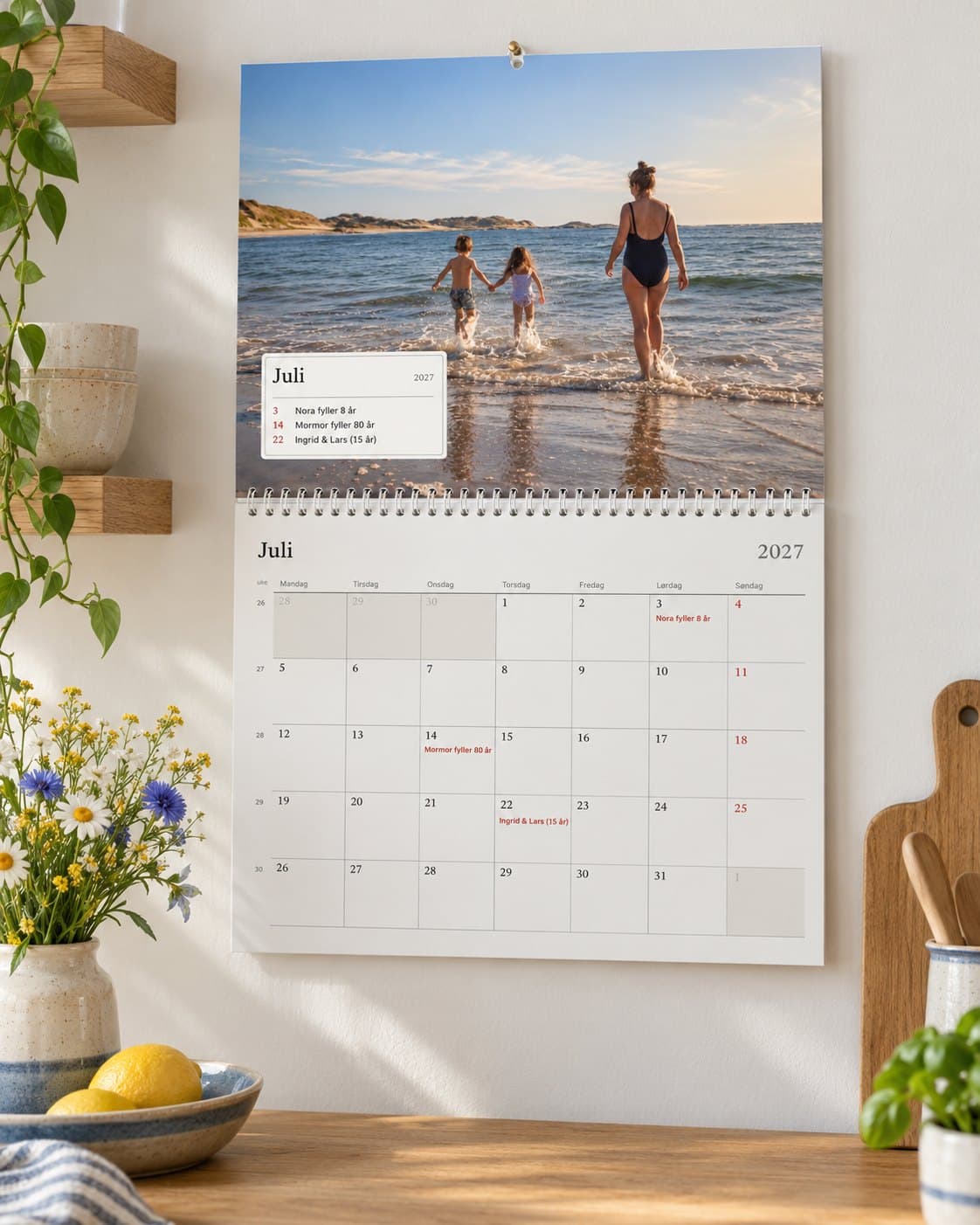 En fotokalender åpnet på juli i et lyst kjøkken: familiens strandbilde over måneden med bursdagene deres