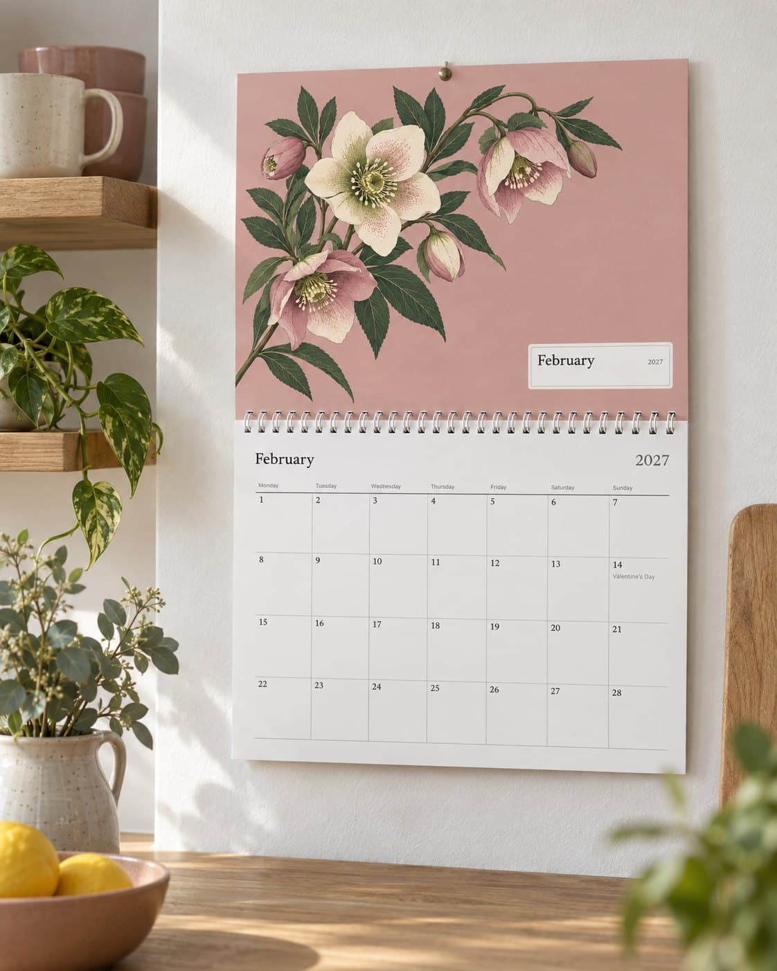 The wall calendar with a flower painting, open at February on a kitchen wall, with the family’s birthdays on the page