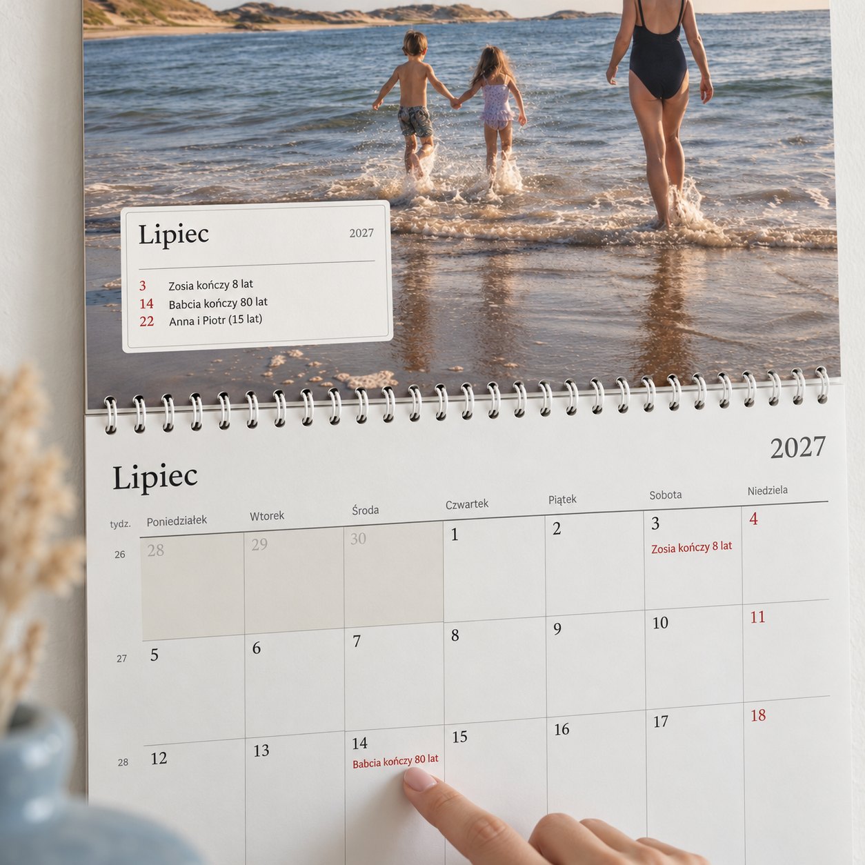 Zbliżenie kalendarza ze zdjęciami: ramka miesiąca pokazuje, kto świętuje, a palec wskazuje 80. urodziny babci
